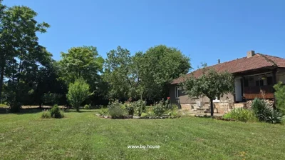 Garden area with grass, flowers, and trees adjacent to a house with a tiled roof and stone steps.
