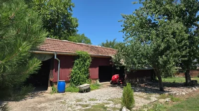 Building with tiled roof and red corrugated metal walls, garden tools and trees around.