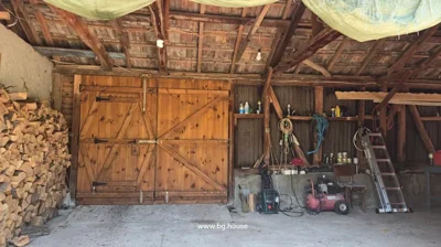 Wooden structure interior with double doors, firewood, and tools.