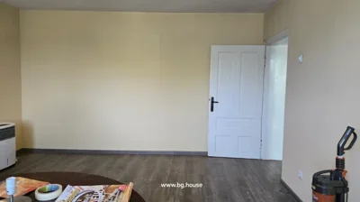 Room interior showing a closed white door, part of a round table with magazines, and a vacuum cleaner with bags on the floor