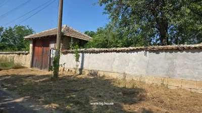 View of the property wall featuring a large wooden gate and a utility pole, with dry grass and trees.