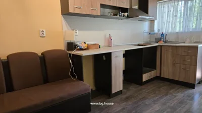 Kitchen space showing wooden cabinets, countertop, sink, range hood, and a brown sofa.