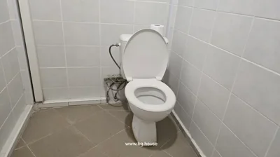 White toilet with open lid, tiled walls and floor, and visible plumbing connections