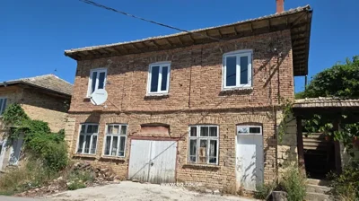 Front view of a two-storey brick house with multiple white framed windows and doors, a satellite dish, and a tiled roof under a clear blue sky