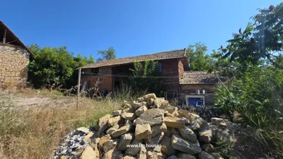 Old wooden and brick house with tiled roof and pile of stones in front under clear blue sky