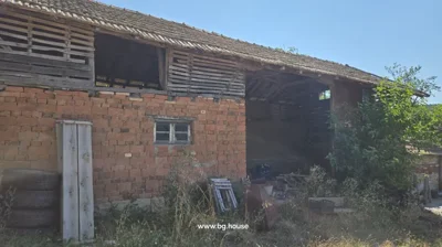 Old brick and wooden building with open upper section, tires, wooden planks, and other items leaning against wall