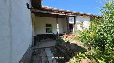 View of covered porch and garden area with white walls, wooden posts, window, and plants growing around