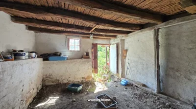 Interior view showing wooden ceiling beams, a small barred window, an open door to the outside, and items on a ledge and floor.