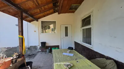 Outdoor covered patio with tiled floor, table with yellow cloth, potted plants, and white door and window on wall.