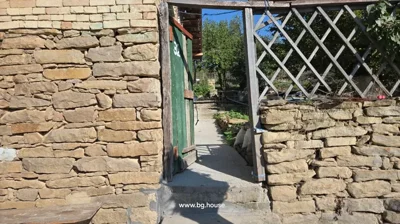 Stone wall with a green wooden gate marked with number 32, next to a wooden trellis structure, under a clear blue sky.
