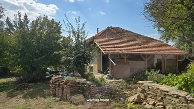 Side view of brick house with tiled roof, garden area with stacked roof tiles and trees