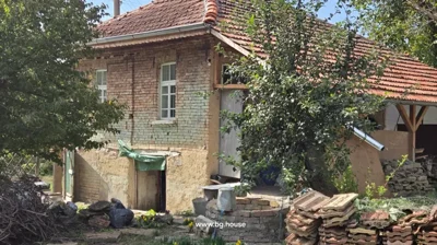 Close-up view of brick house with tiled roof, trees, and stacked roof tiles in the garden