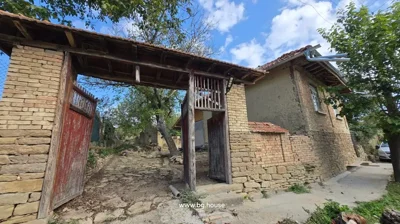 Old wooden gate and stone wall entrance leading to brick house with tiled roof and garden