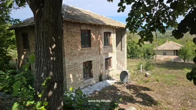 Two-storey brick house with tiled roof and four windows visible, surrounded by trees and greenery