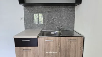A kitchen sink with a metal faucet, countertop, and cabinets below, set against a white wall with a gray marble-patterned backsplash.