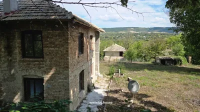 Brick house with yard, satellite dish, trees, and distant hills in background.