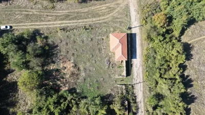 Top-down view showing the house with a red tiled roof, grassy land, trees, and a dirt road with a white car.