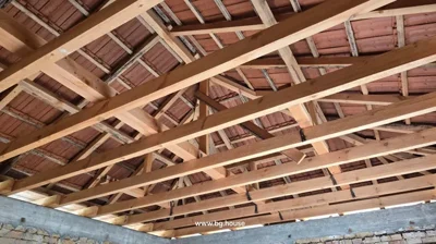 Interior view of wooden roof trusses and red roof tiles inside a building under construction