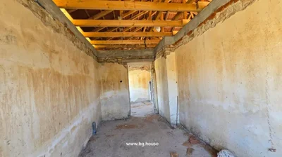 Room interior showing exposed wooden roof beams, bare plaster walls, and a rough concrete floor with some debris.