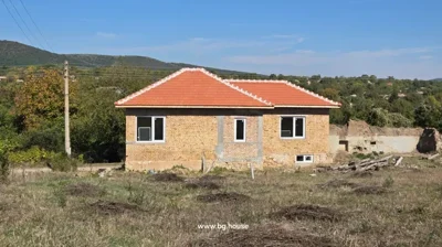 Brick house with red tiled roof and three white-framed windows, with hills and trees in the background.