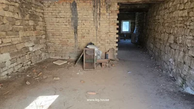 Room with stone and brick walls, construction materials on the floor, and a small window at the end.