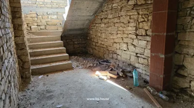 Stone walls and concrete stairs inside a building under construction with scattered bricks and plastic bottles on the floor