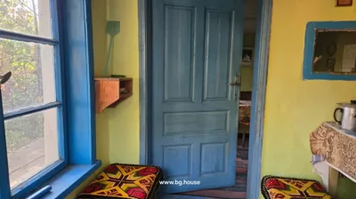 Room interior with blue door and window frame, yellow walls, wooden shelf, and colorful cushion on bench.