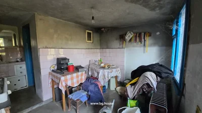 Room interior showing a table with a tablecloth, chairs, a coffee machine, and other household items.