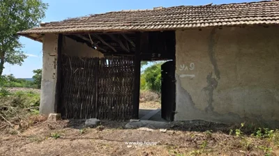 Entrance gate featuring a wooden door and woven fence, with some markings on the plaster wall beside it.