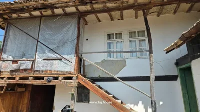 Close-up view of wooden stairs leading to the upper floor of a traditional Bulgarian house with white walls, windows, and a covered balcony area.