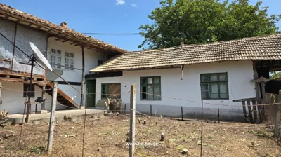 View of a traditional Bulgarian house with white walls, green window frames, wooden stairs, and a satellite dish attached to the side.