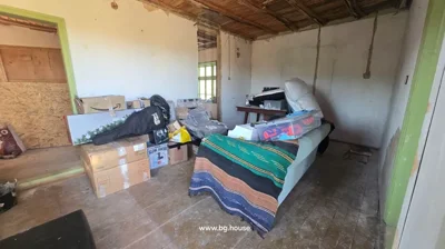 Room interior showing wooden ceiling, white walls, and various household items and boxes scattered around