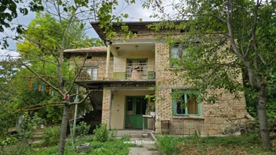 Two-storey brick house with green doors and windows, surrounded by trees and garden with clothesline and clothespins.