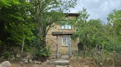 Front view of two-storey brick house with wooden gate and fence, surrounded by trees and garden.