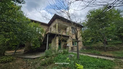 Front view of two-storey brick house with green doors and windows, garden with trees and clothesline with clothespins.