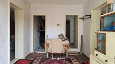 Interior room with white walls, carpet on floor, small table with cloth and chair, two doorways leading to other rooms