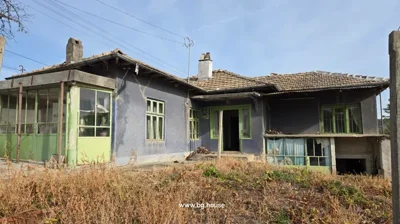 Closer view of the house showing green framed windows and doors, with dry vegetation in front.